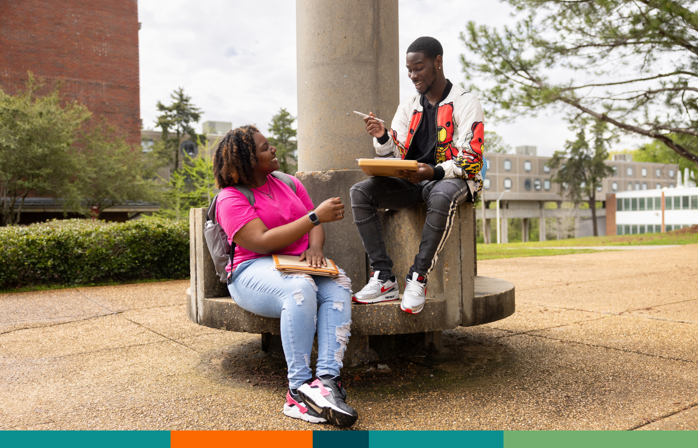 Two black students sitting on the university campus and chatting.